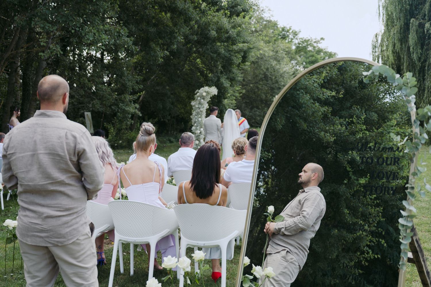 Small outdoor wedding ceremony takes place in a lush garden setting with a white wedding arch and decorations.