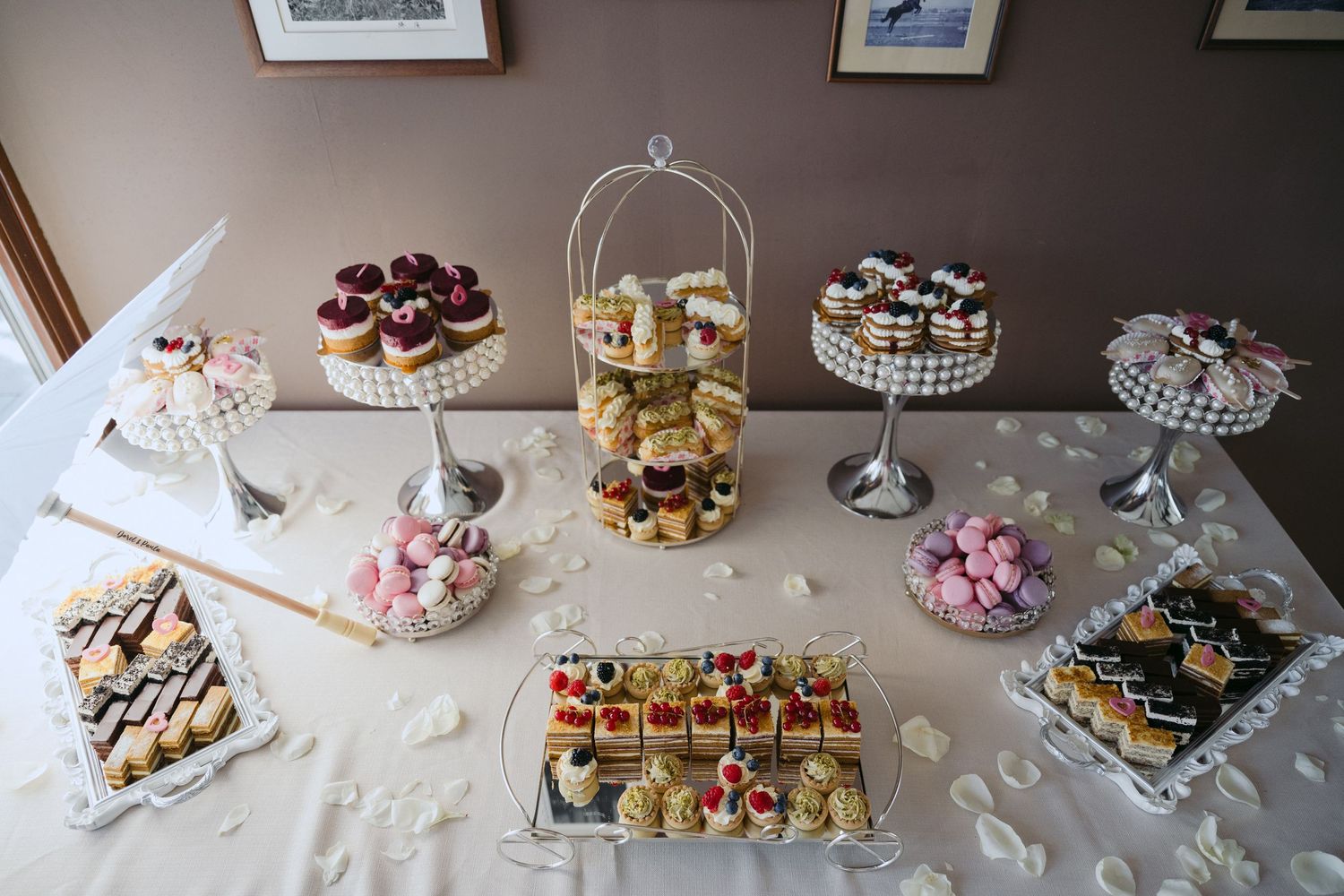 Elegant dessert table with crystal cake stands displays an assortment of pastries, cupcakes, and bite-sized treats.
