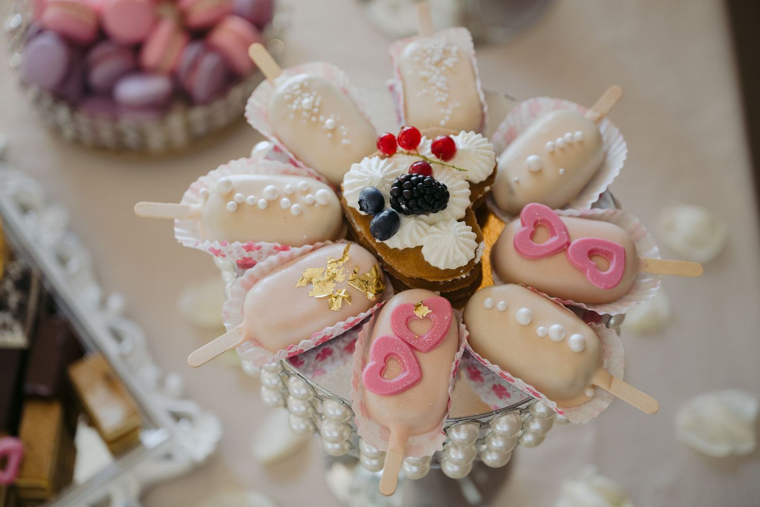 Pink and white cake pops decorated with hearts and sprinkles arranged in a circular pattern on a pearl display stand.