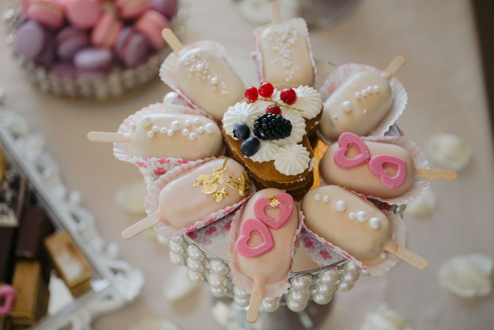 Pink and white cake pops decorated with hearts and sprinkles arranged in a circular pattern on a pearl display stand.