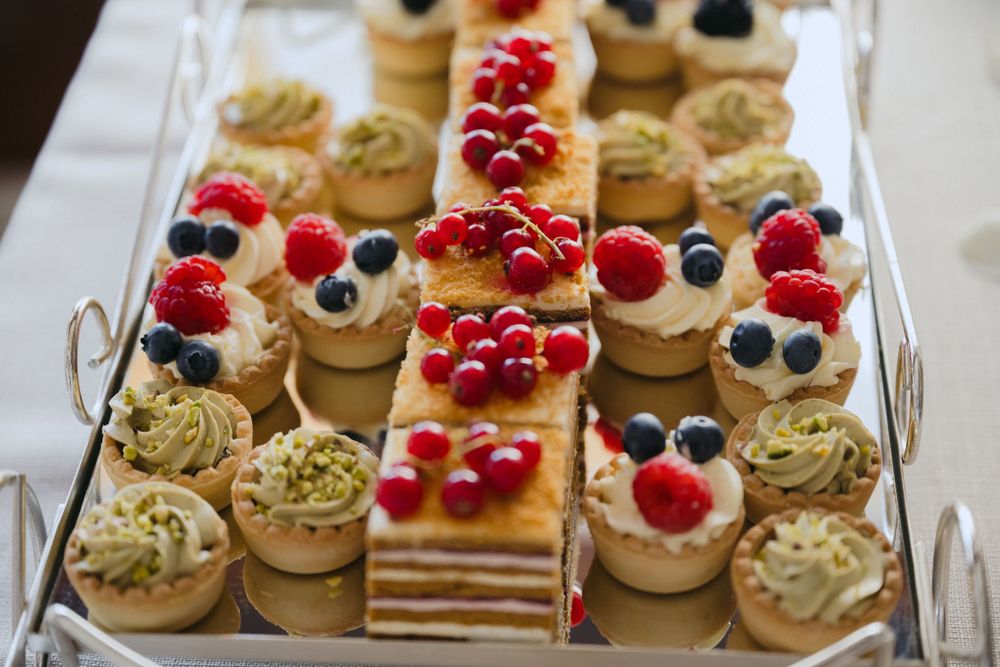 Assorted mini desserts and petit fours with berries and pistachios arranged on a white serving tray.