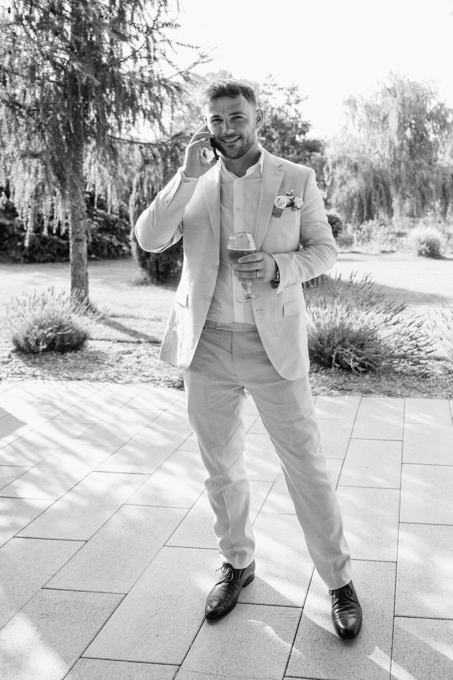 Black and white photo of person in light colored suit talking on phone while standing outdoors on stone patio.