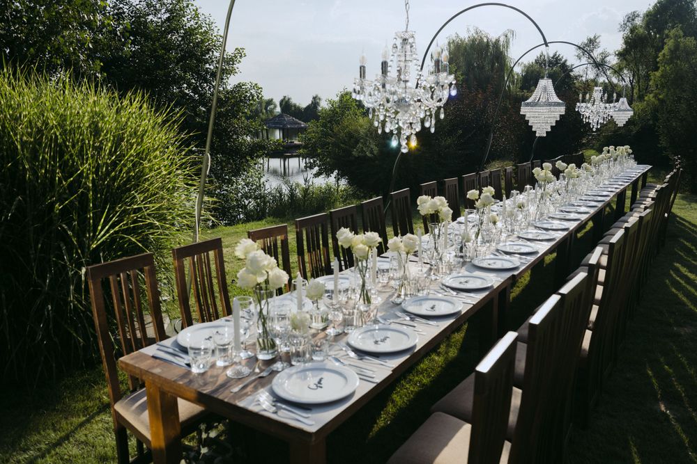 Elegant outdoor dining table with crystal chandeliers set for a garden wedding reception with white place settings.