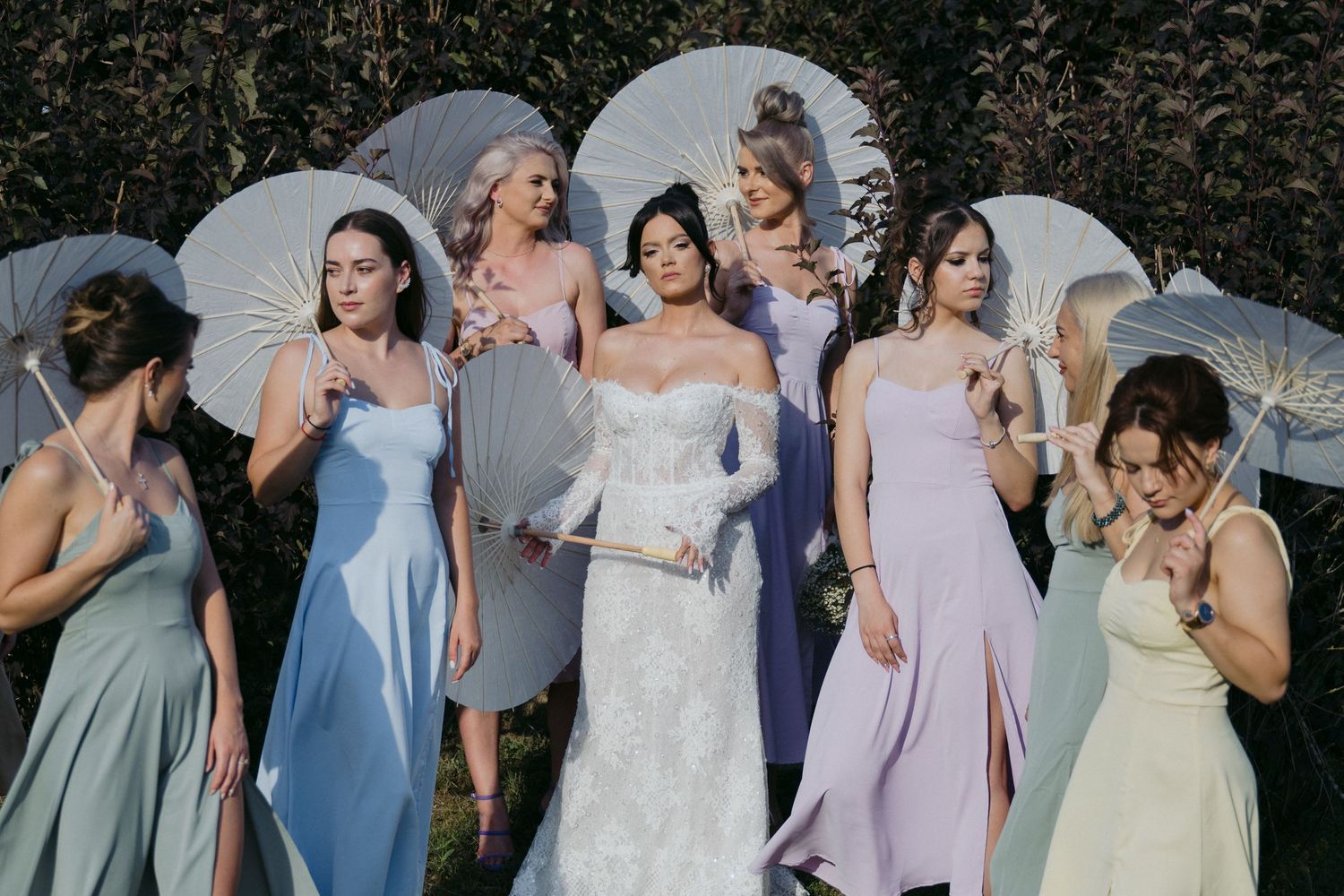 Bridal party in soft pastel gowns and white umbrellas share a candid moment during outdoor wedding photos.