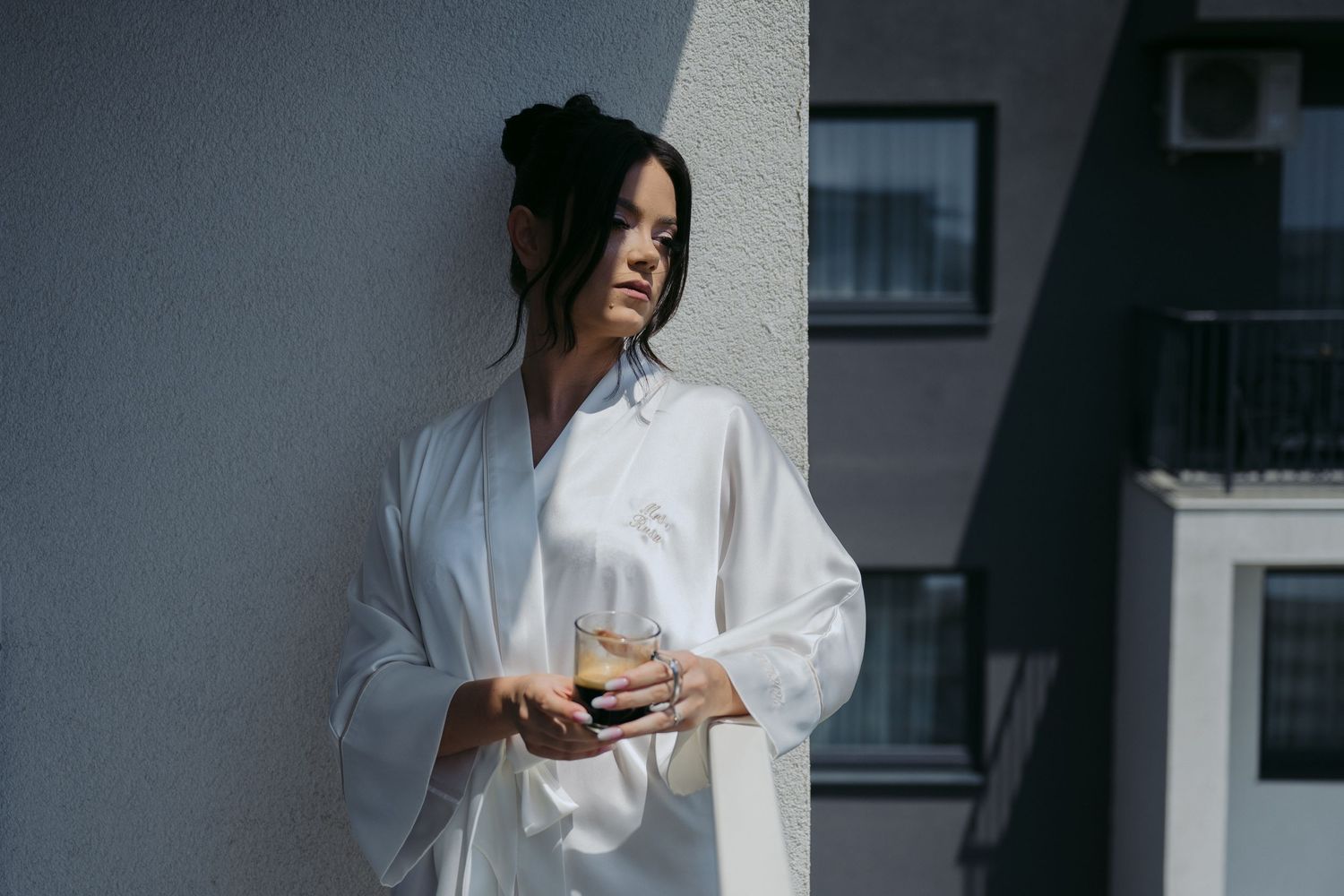 Person wearing an oversized white shirt stands against a concrete wall in moody lighting.