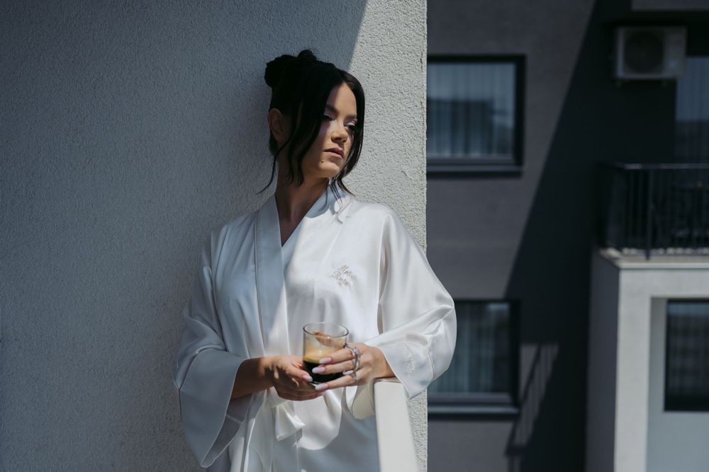 Person wearing an oversized white shirt stands against a concrete wall in moody lighting.
