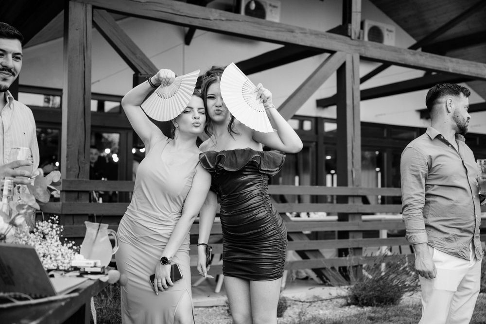 Two friends in dresses laugh and pose together at an outdoor event in black and white photography.