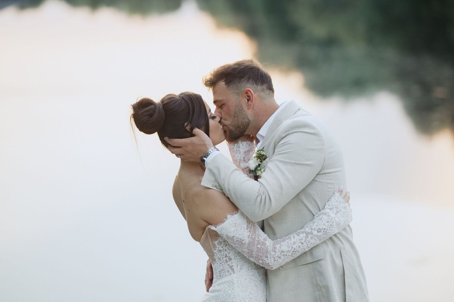 A romantic wedding couple embraces in front of a misty waterfront during their intimate outdoor ceremony.