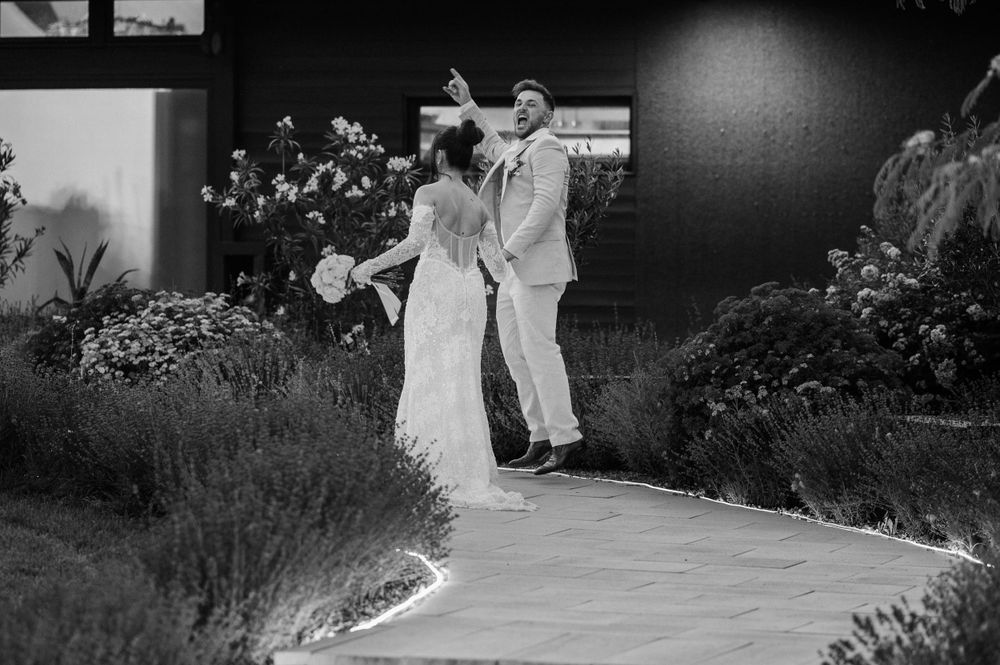 A black and white wedding photograph showing a couple dancing together on a garden pathway.