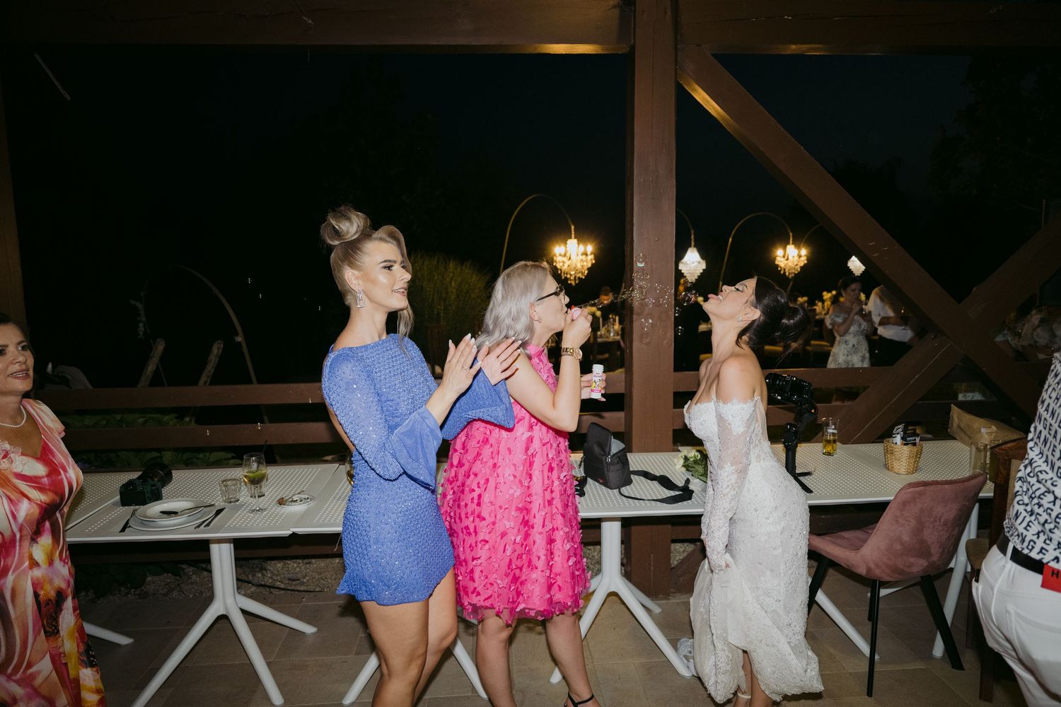 People dancing and socializing at a nighttime party venue with decorative lighting and white tables.