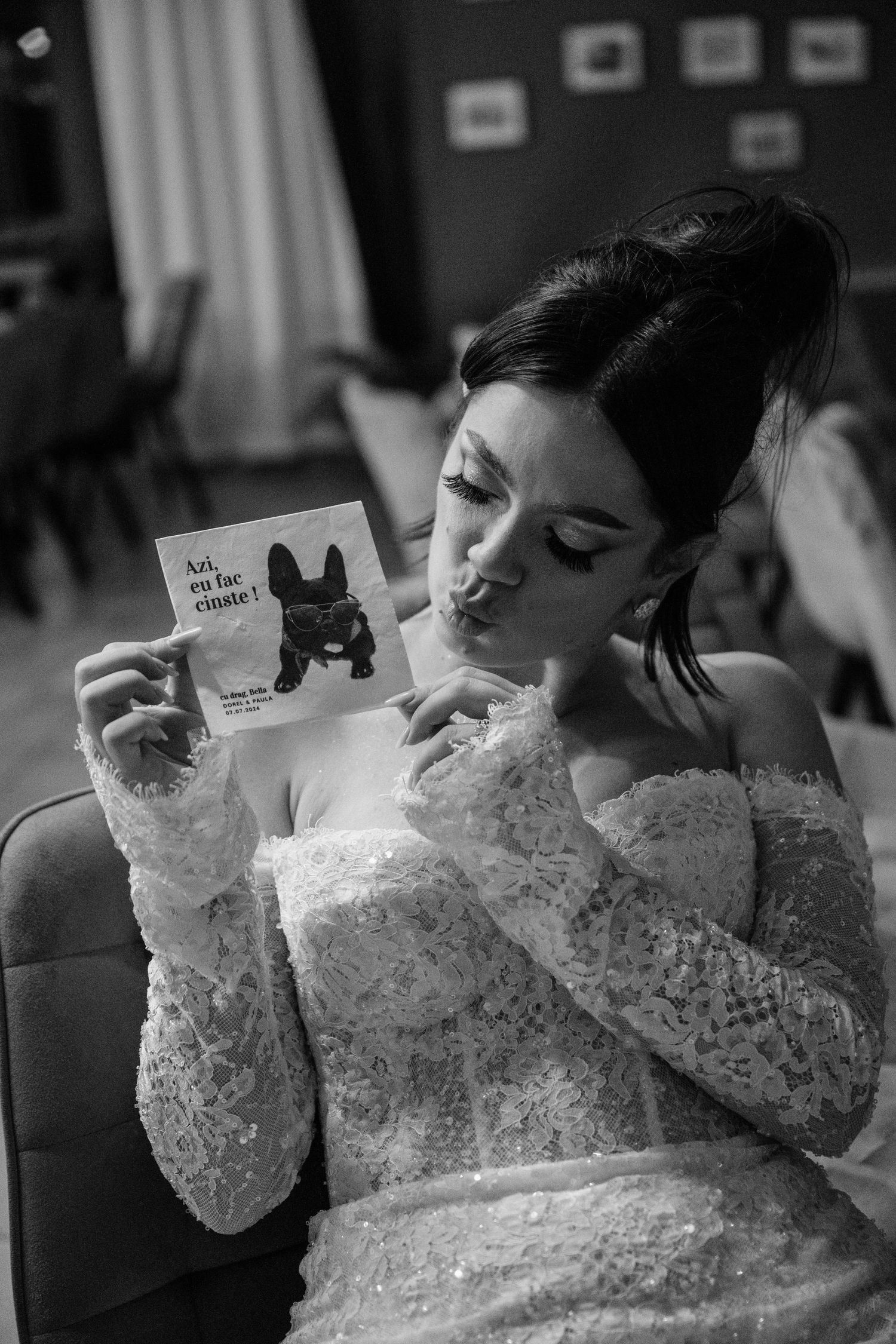 A bride in a lace dress holds up a cute dog-themed card during wedding preparations in black and white.