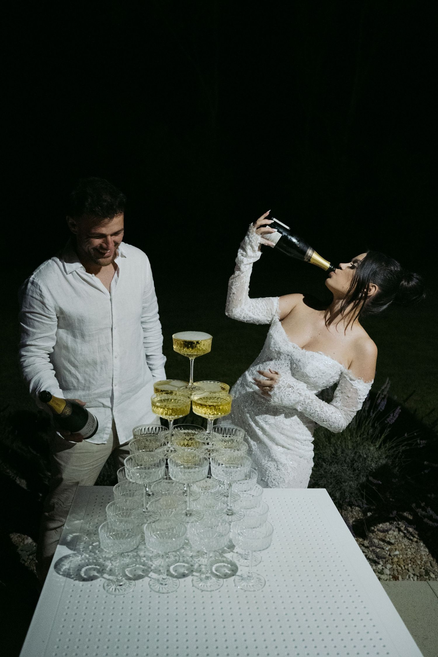 Couple celebrating at a wedding reception with champagne tower at night.