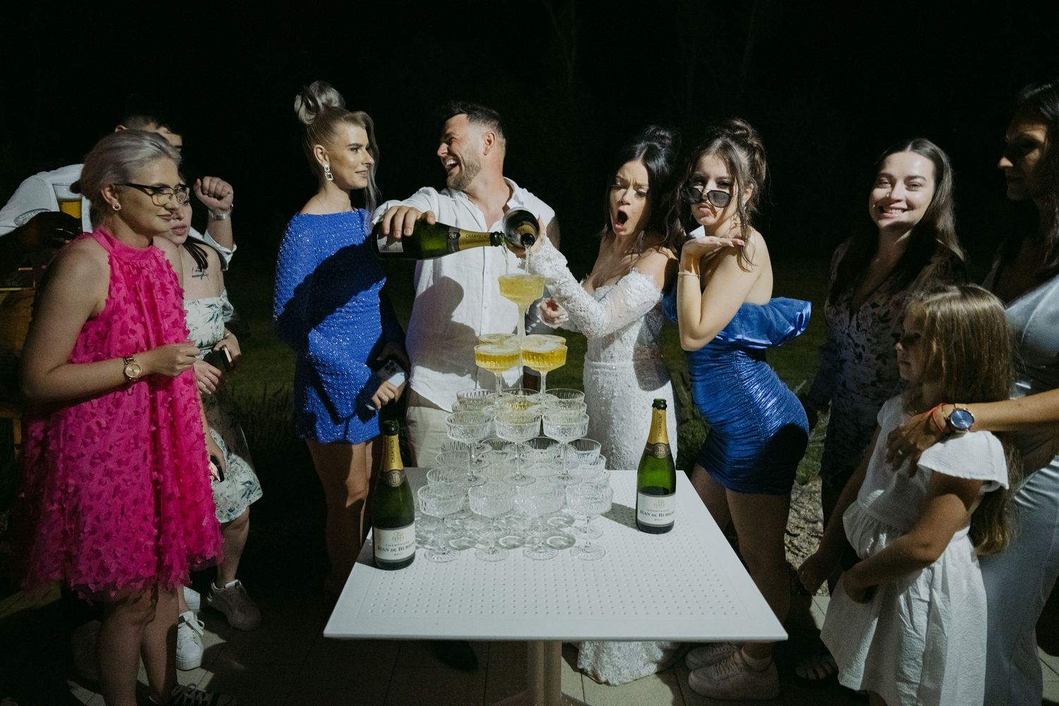 Group celebrating with champagne at night party pouring drinks and having fun together.