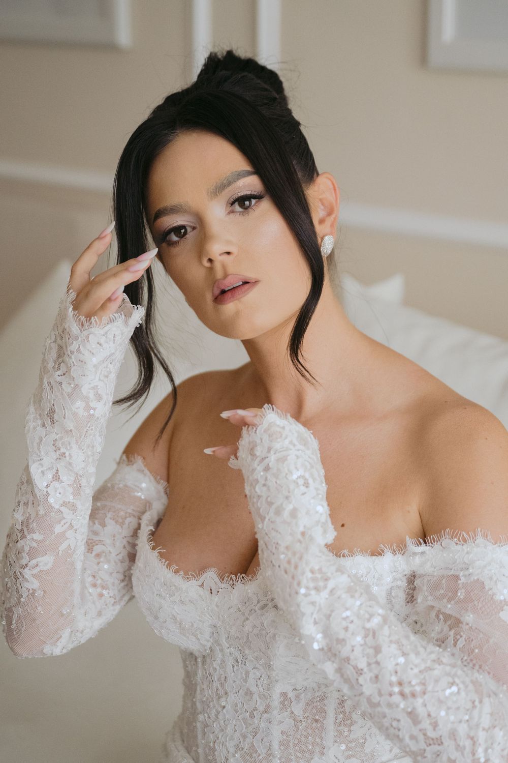 Elegant off-shoulder white lace wedding dress with long sleeves and delicate bridal details captured in soft indoor lighting.