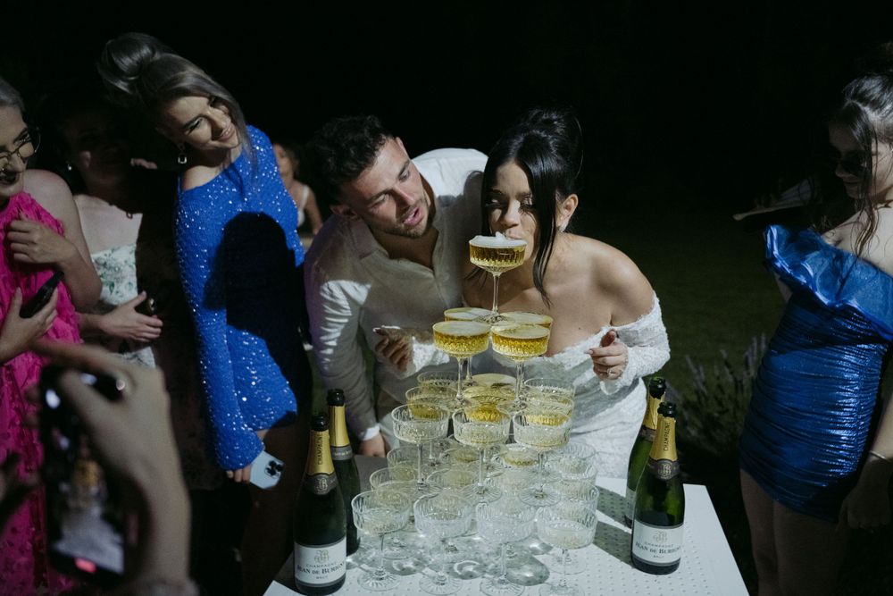 People celebrating at a nighttime party with champagne glasses and bottles on a table illuminated in dark lighting.