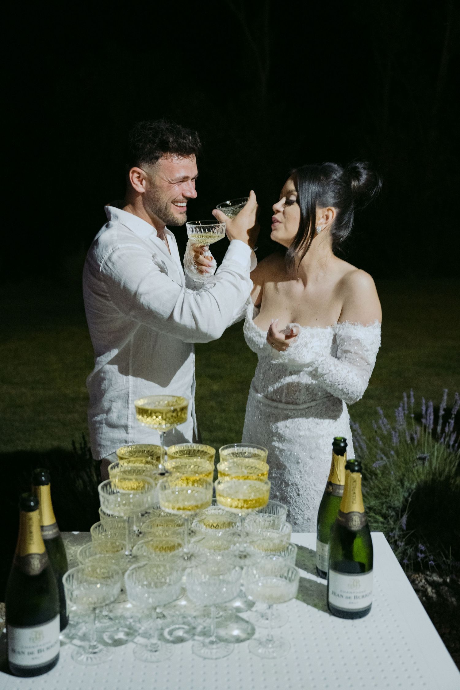 A celebratory champagne toast at an elegant outdoor wedding reception with multiple flutes arranged on a white table.
