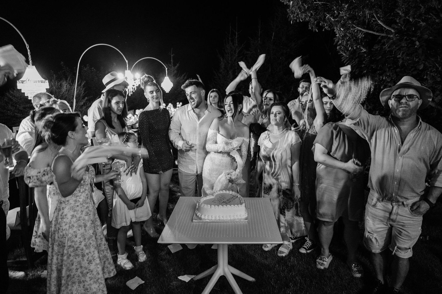 Wedding guests hold sparklers while gathered around a white table during an outdoor nighttime celebration.