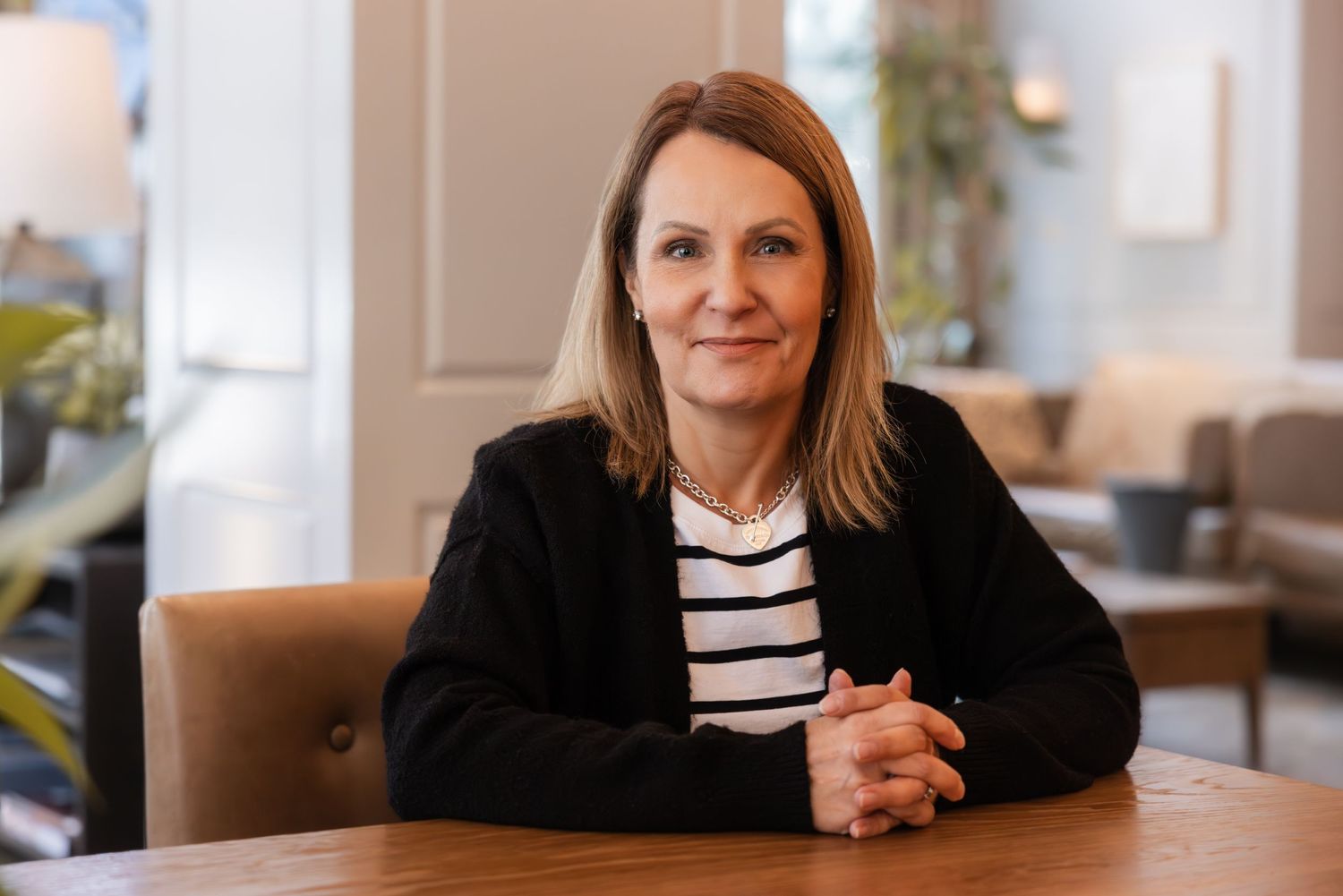 Professional wearing a black cardigan over striped shirt sits at wooden table in modern office interior.