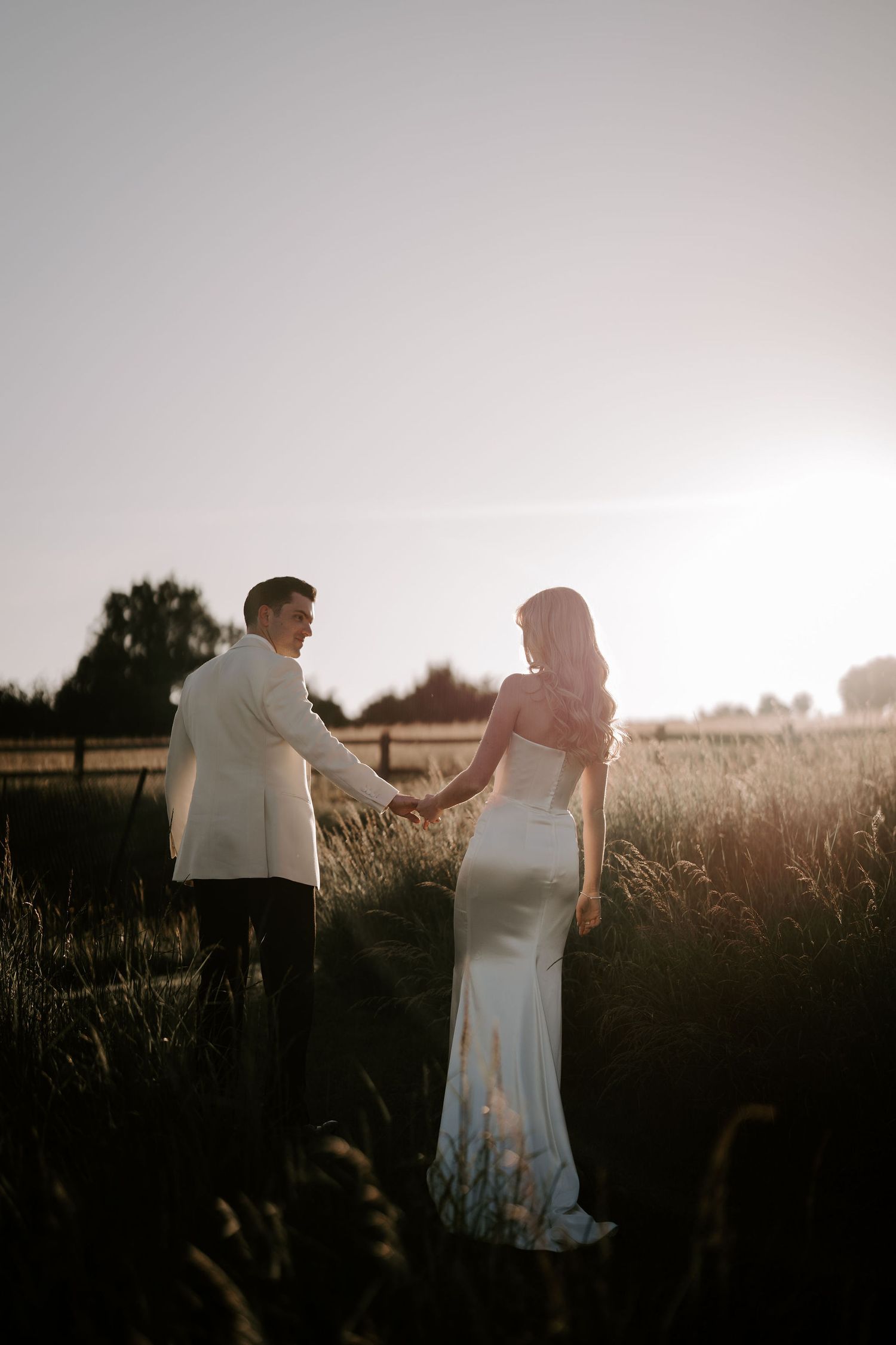 groom leading and looking back at his bride into the sunset at hamswell house wedding in bath