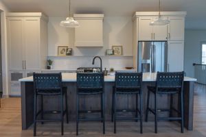 Modern white kitchen with dark navy bar stools and pendant lights at a large kitchen island featuring quartz countertops.