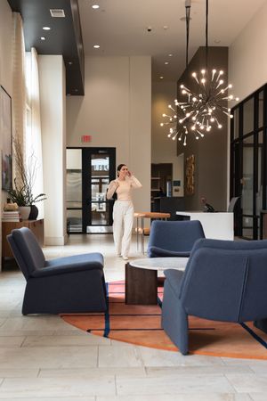 Modern hotel lobby interior with navy blue chairs, decorative sputnik chandelier, and stone tile flooring.