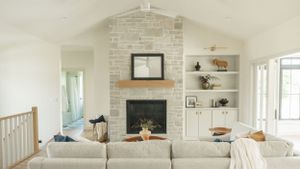 Modern living room interior with stone fireplace, white built-in shelving, and comfortable neutral sectional sofa.