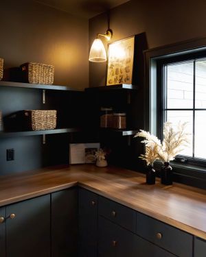 Modern kitchen featuring dark navy cabinets, butcher block countertops, floating shelves and pampas grass decor by window.