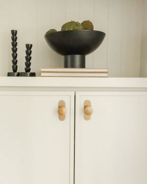 Modern white cabinet with wooden knobs displays a black pedestal bowl and decorative twisted black candlesticks on top.