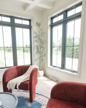 Cozy corner reading nook with red velvet armchairs and large windows overlooking a scenic view, accented by a potted plant.