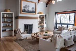 Modern coastal living room with floating shelves, fireplace, and cozy seating arranged on light hardwood floors.