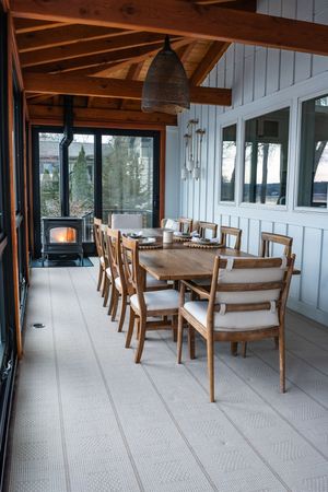 Rustic enclosed porch with wood beams, dining table set, and pendant lighting overlooking outdoor views.