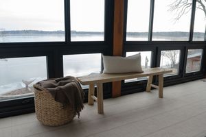Modern minimalist seating area with bench and woven basket against large windows overlooking a serene lake view.
