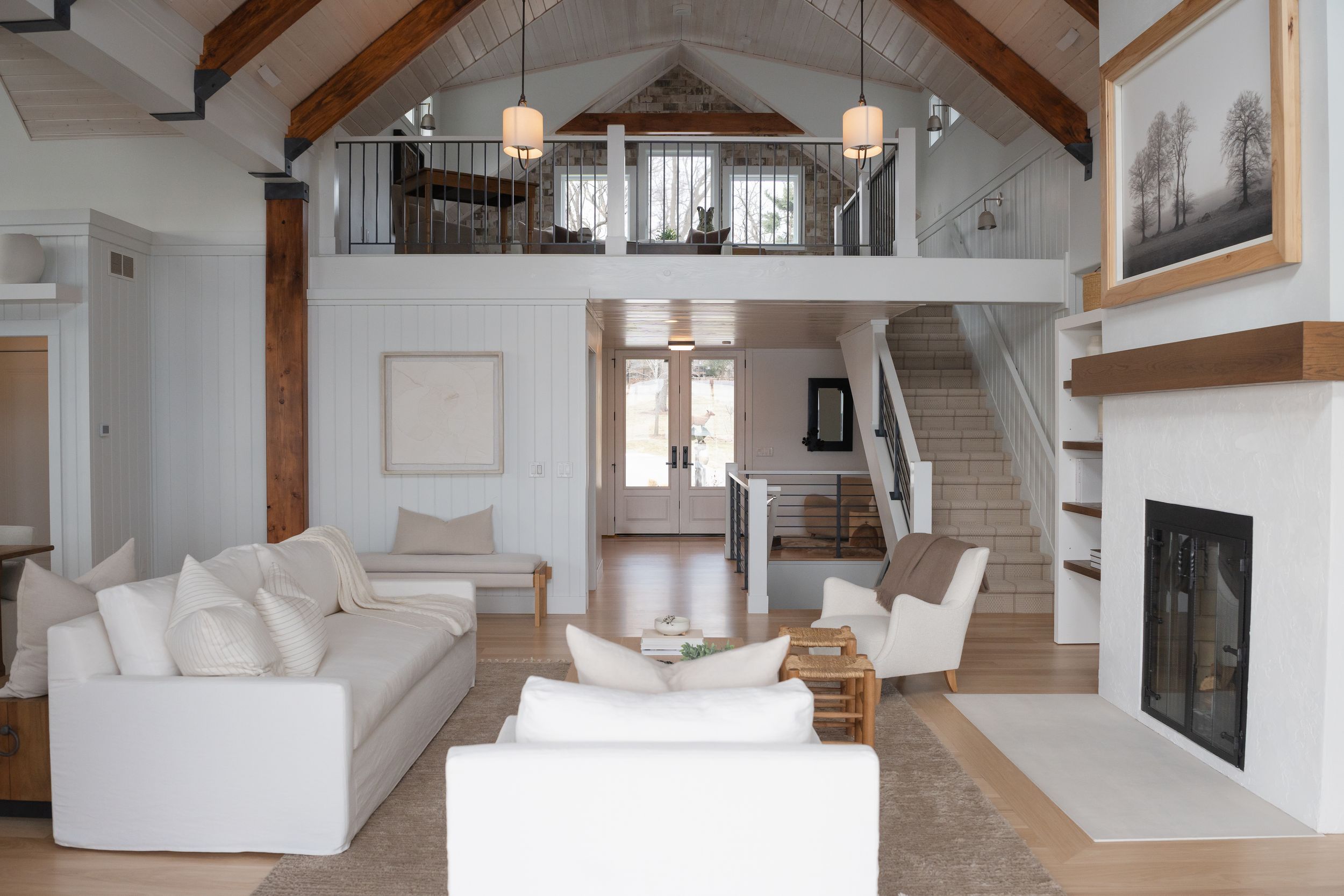 Two-story beach house interior with white furnishings, vaulted ceiling, and exposed wooden beams.