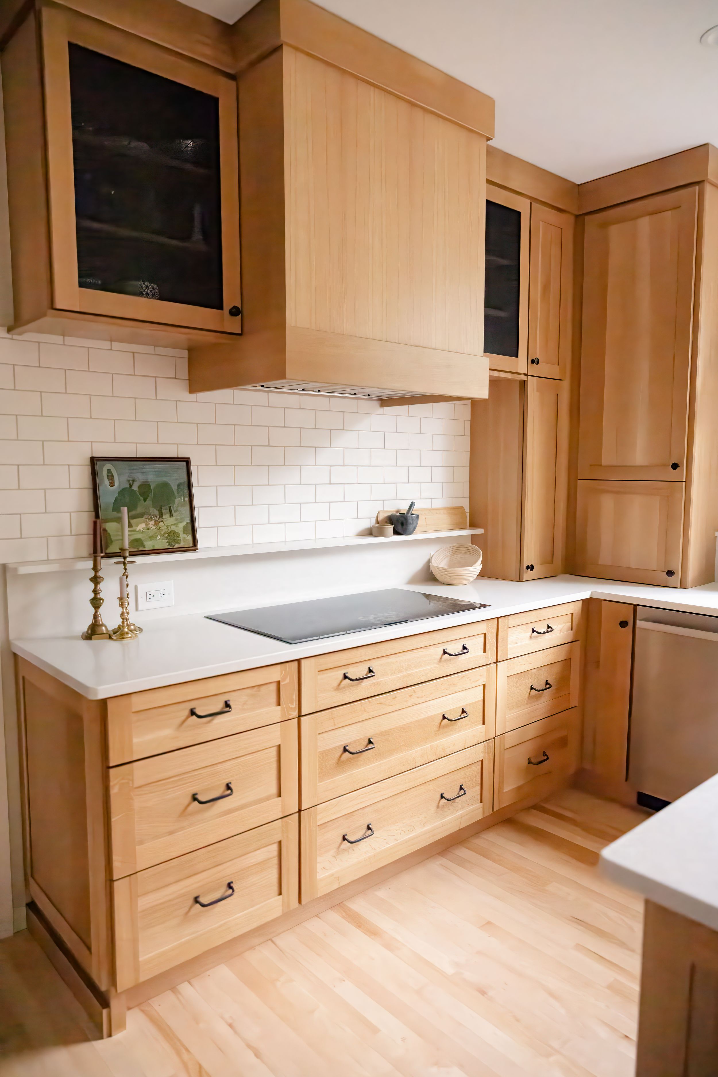 Modern kitchen with light wood cabinetry, white subway tile backsplash, and white countertops featuring inset cooktop.