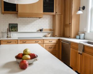 Modern kitchen with warm wood cabinets, white subway tile backsplash, and fresh apples on white countertop.