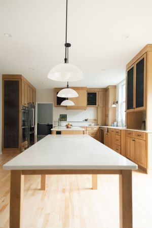 Modern kitchen with light wood cabinets, white countertops, and pendant lights above a long central island.