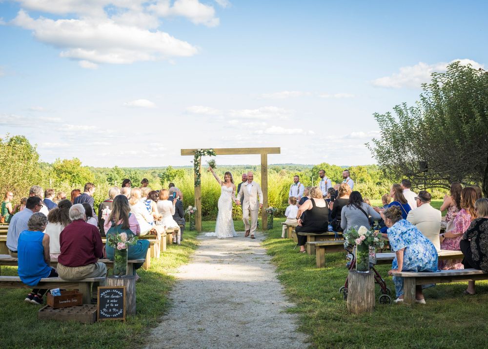 An outdoor wedding ceremony setup with rows of wooden benches and a natural pathway leading to an altar area.