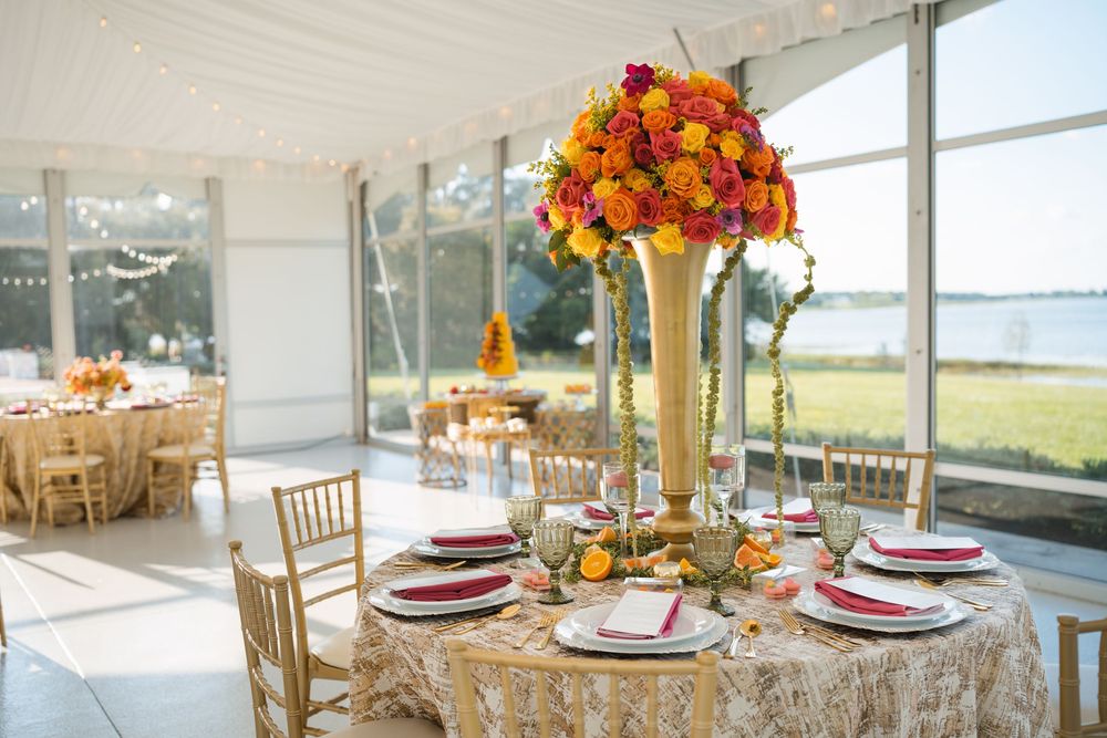 Elegant seasonal table settings with floral centerpieces and gold chairs in a bright waterfront event space.