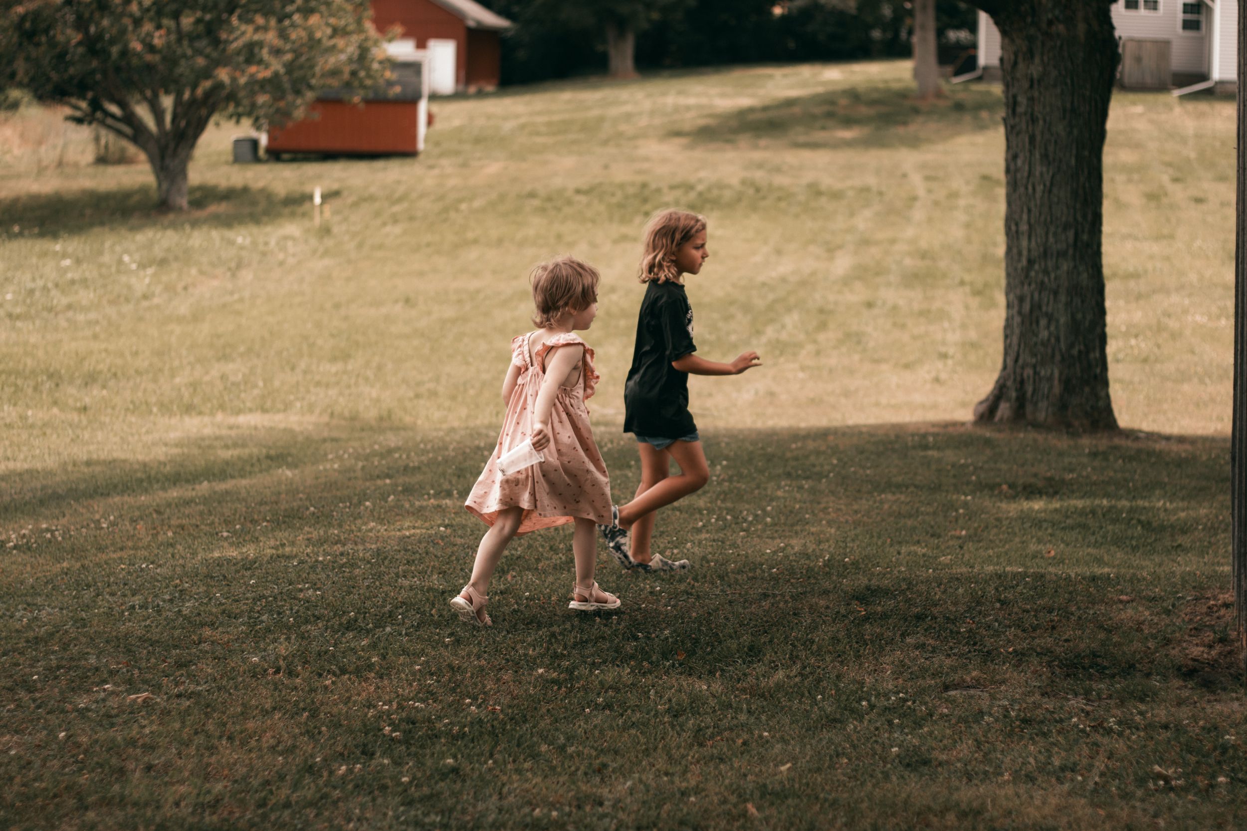 A person in a pink dress runs and plays on a grassy hillside on a sunny summer day.
