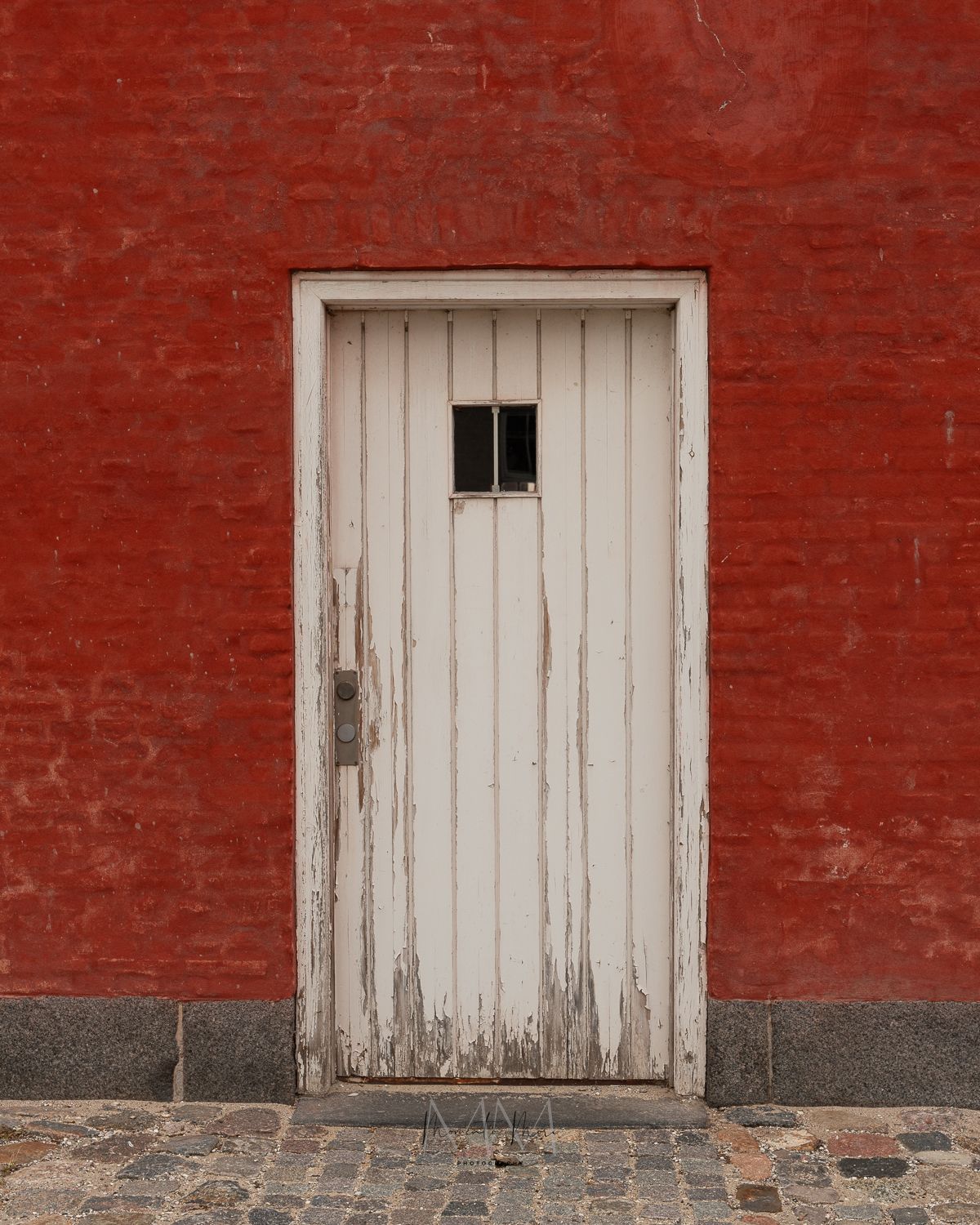 A worn white door is framed by tomato red bricks in a Copenhagen neighborhood.