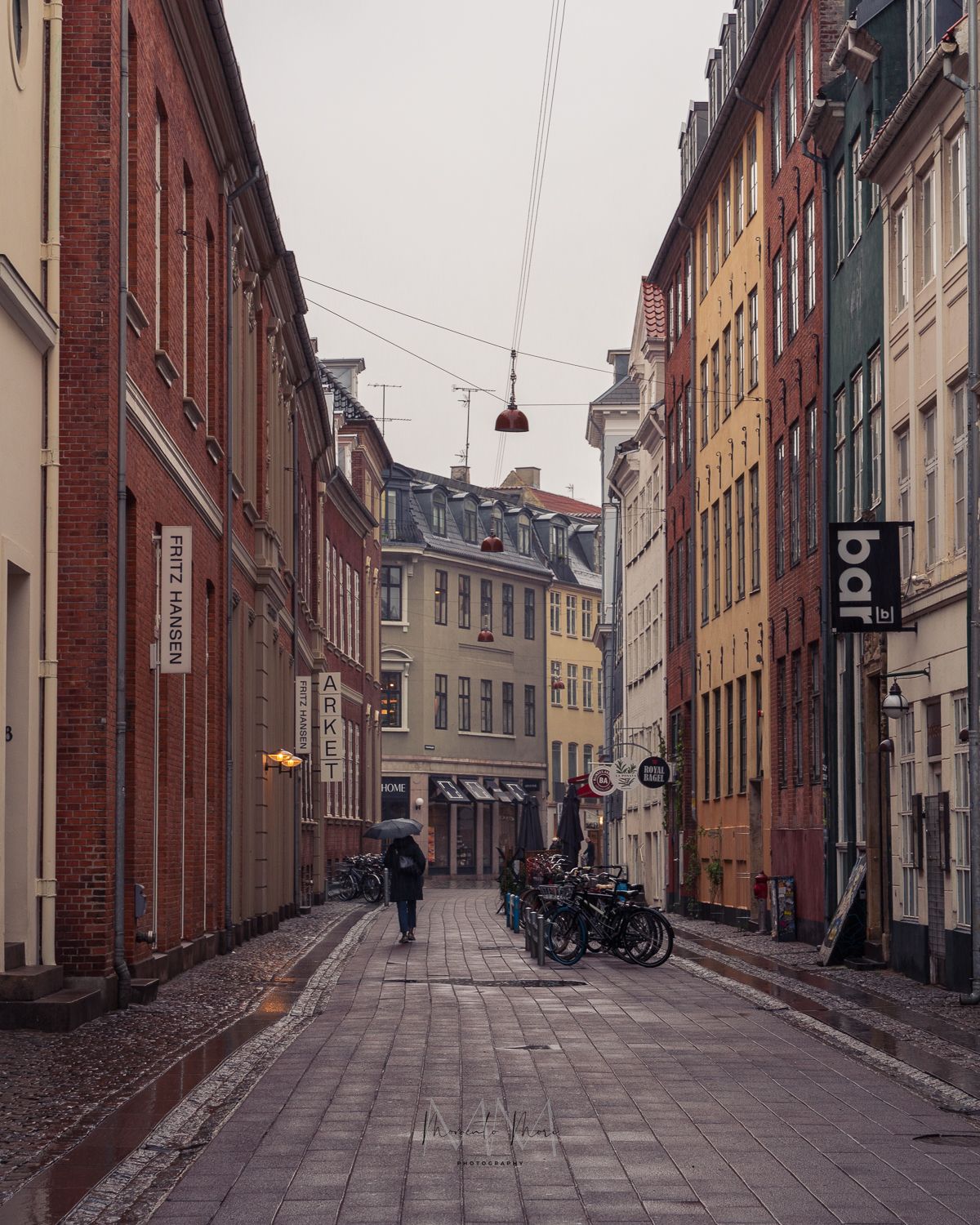 A street photograph capturing a local walking with an umbrella along a cobblestone street lined with colorful buildings on a rainy day