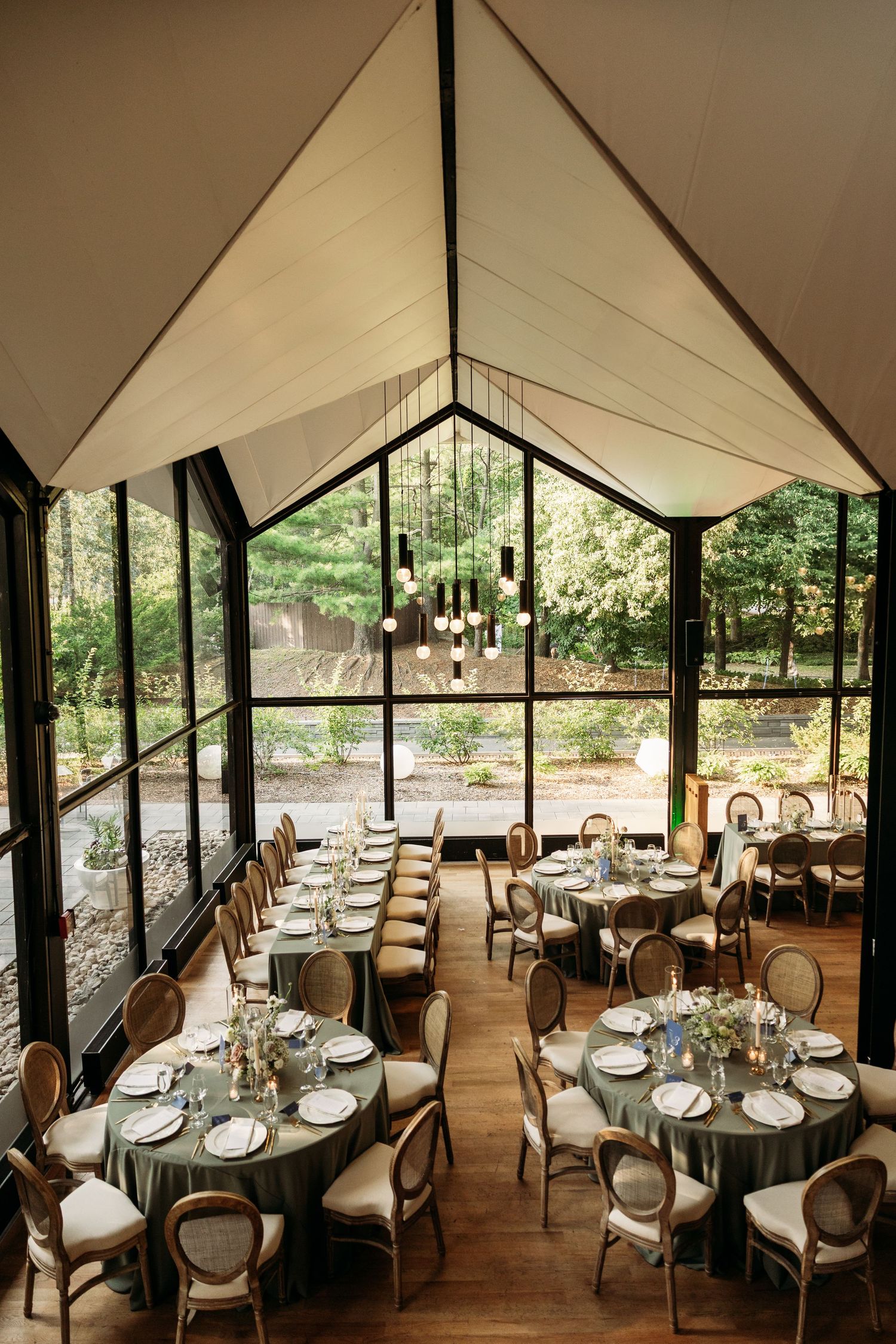 Elegant outdoor tent dining setup with round tables and natural lighting overlooking scenic landscape views.