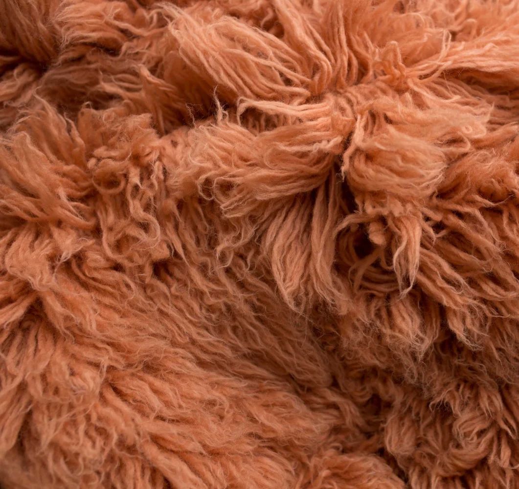 Gray fluffy shag pillow cushion with long textured fibers on a neutral beige background.