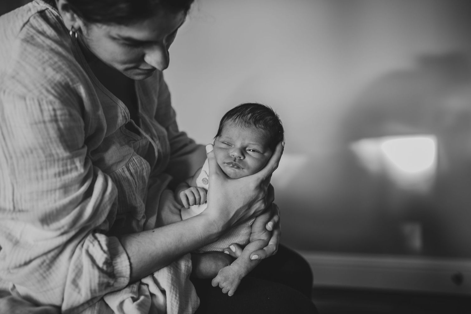 A tender black and white photograph shows an adult carefully holding and gazing at a newborn baby in soft lighting.