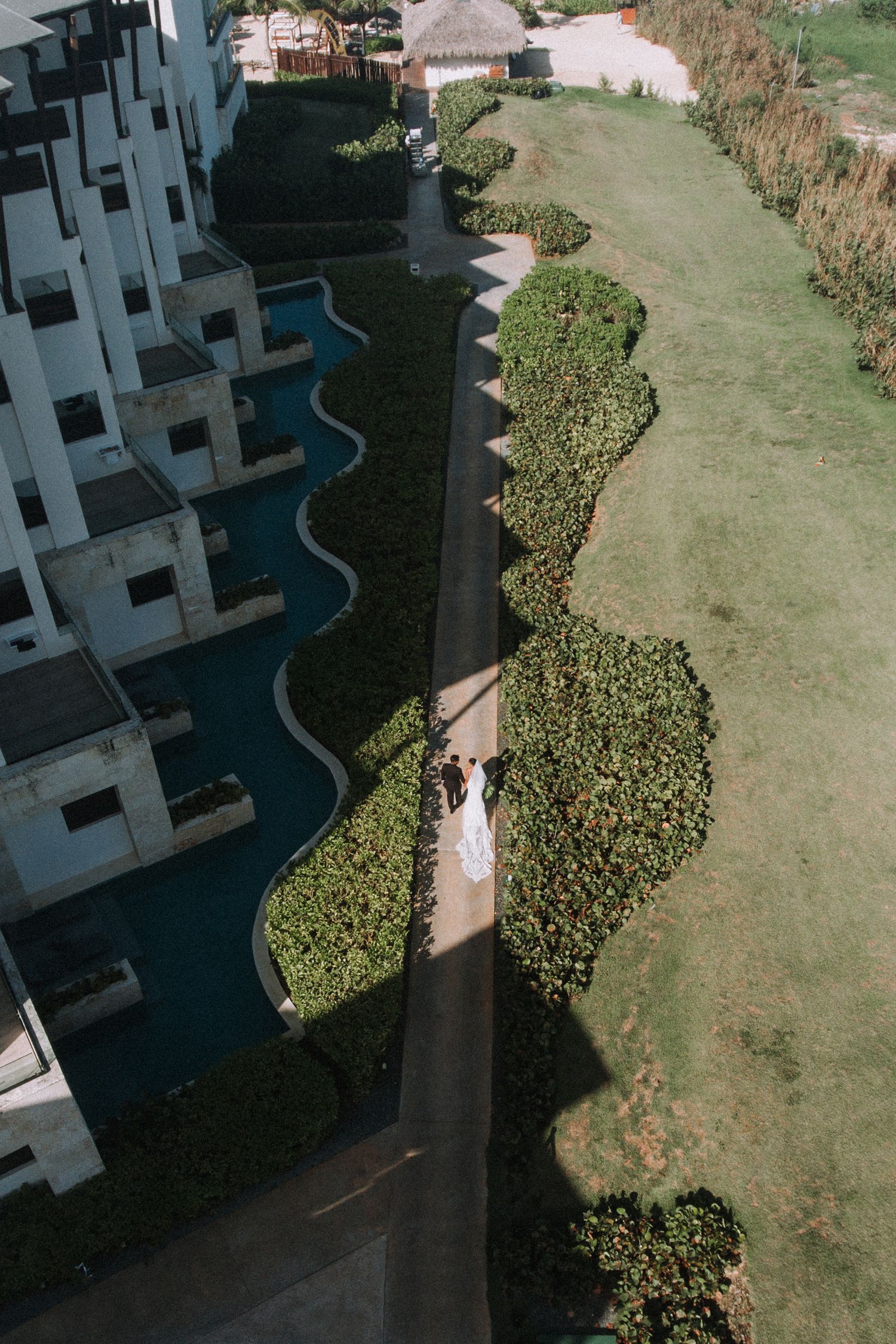 Aerial view of newlyweds walking along a path between modern buildings and landscaped gardens.