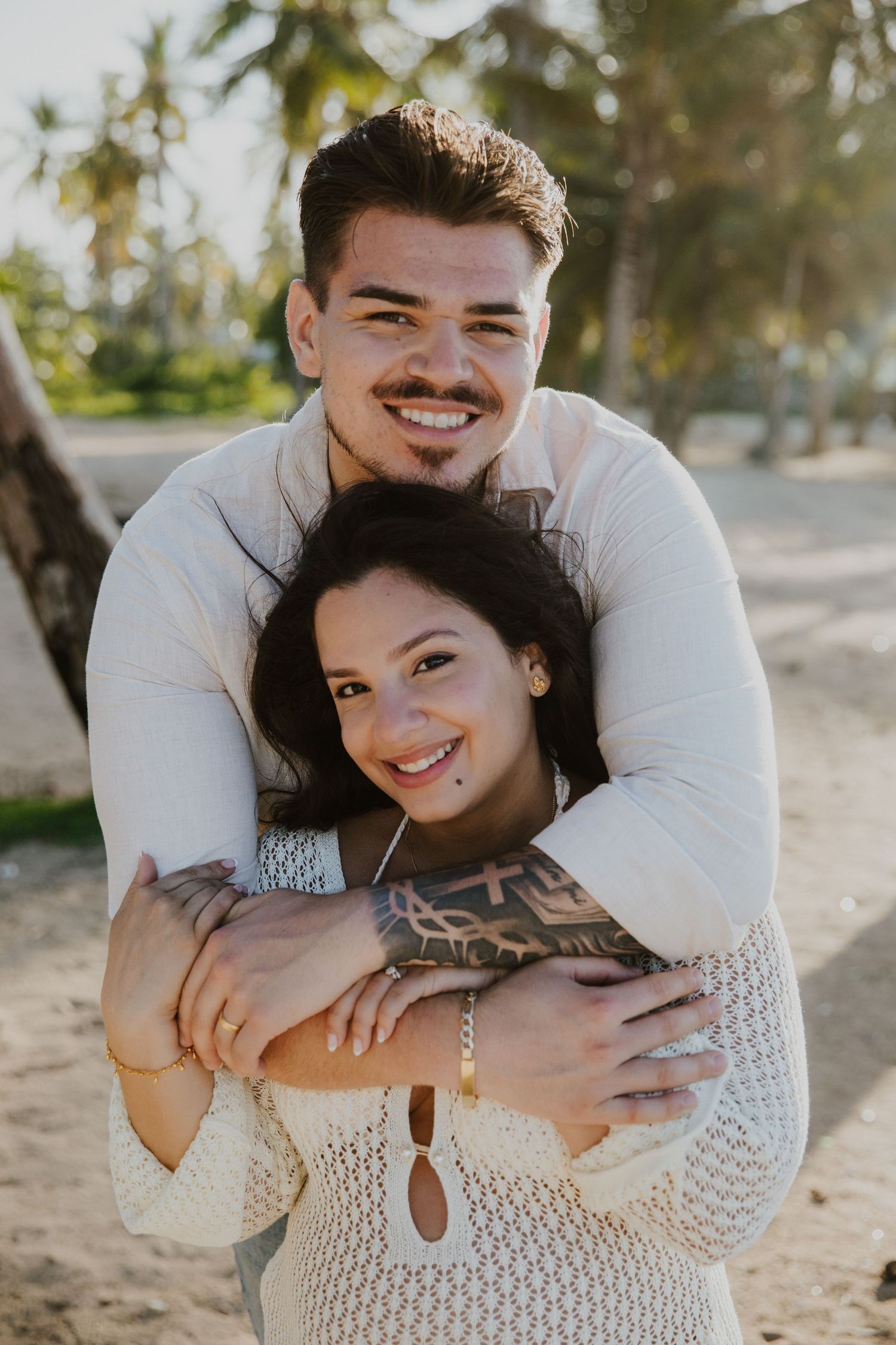 A happy couple embracing on a sunny tropical beach with swaying palm trees.