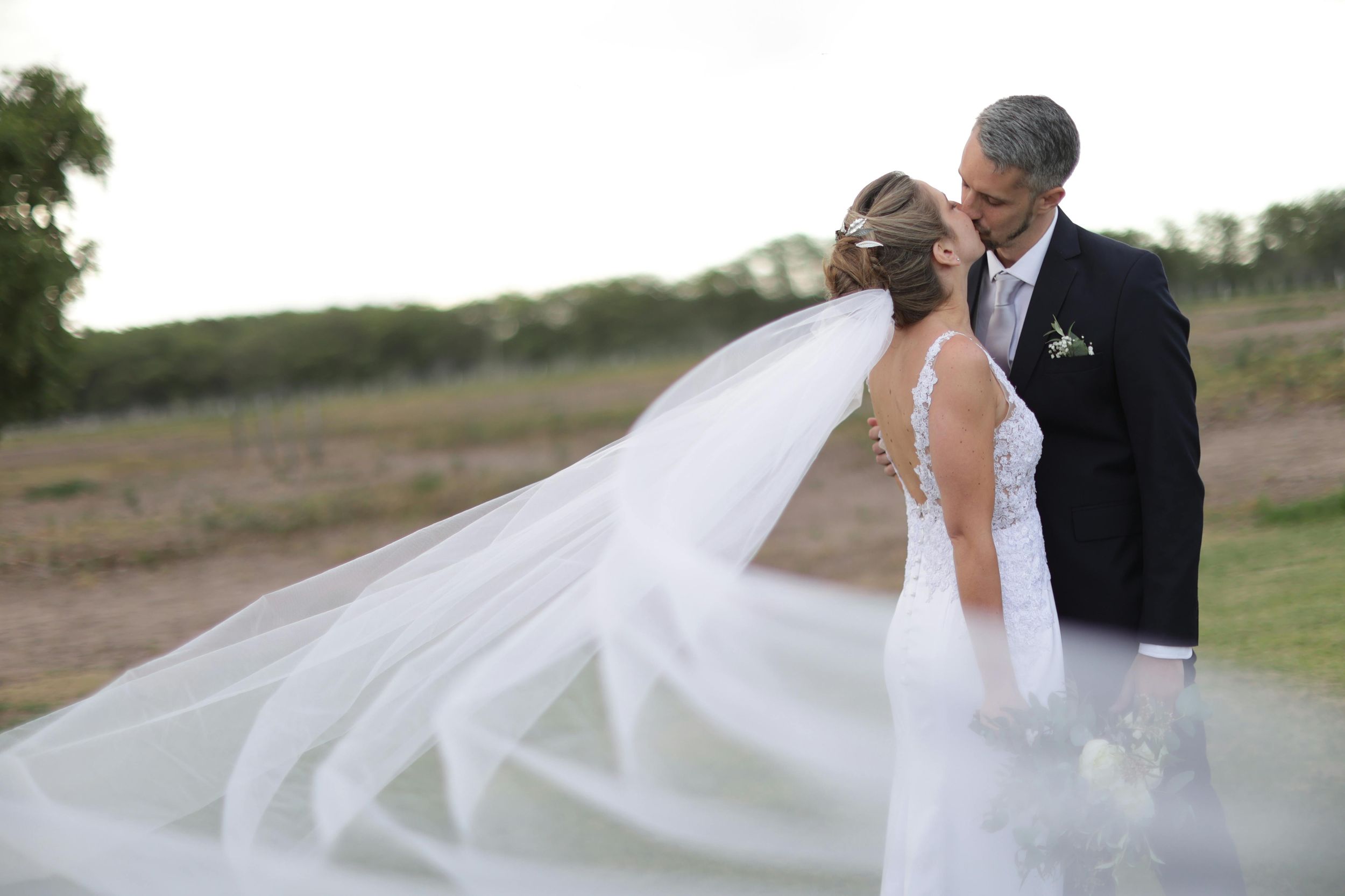 A flowing white wedding veil billows in the breeze across a scenic outdoor landscape during a wedding photoshoot.