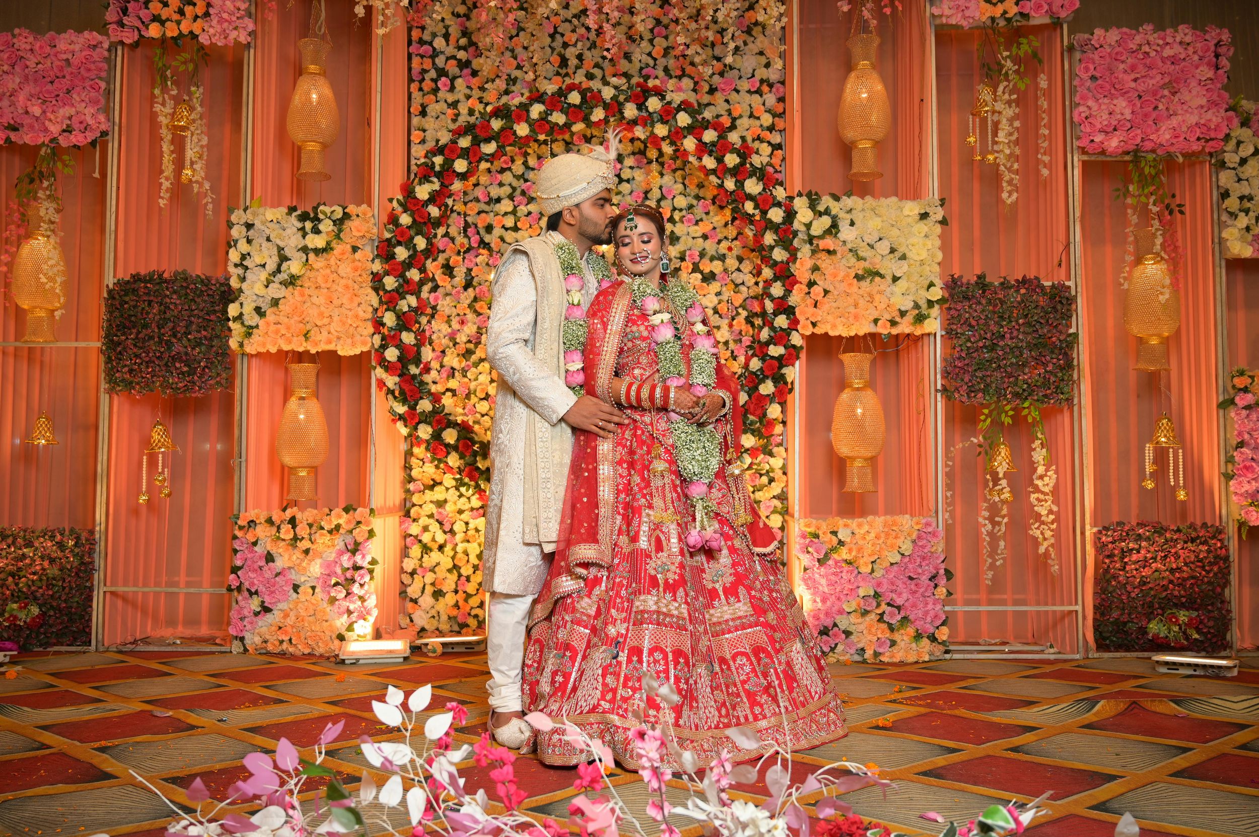 Luxurious Indian wedding venue decorated with pink and gold floral arrangements, drapes, and elegant lighting.