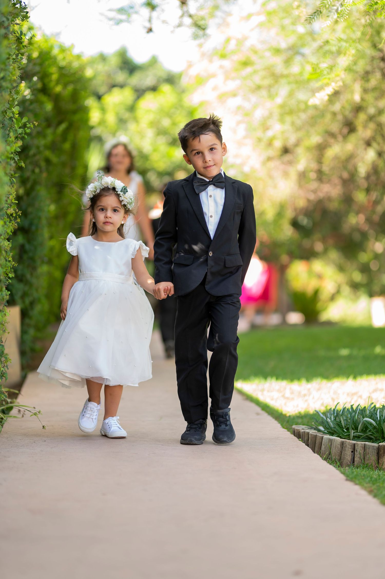 Two adorable children in formal wedding attire sitting and playing together on stone steps in a sunny garden setting.