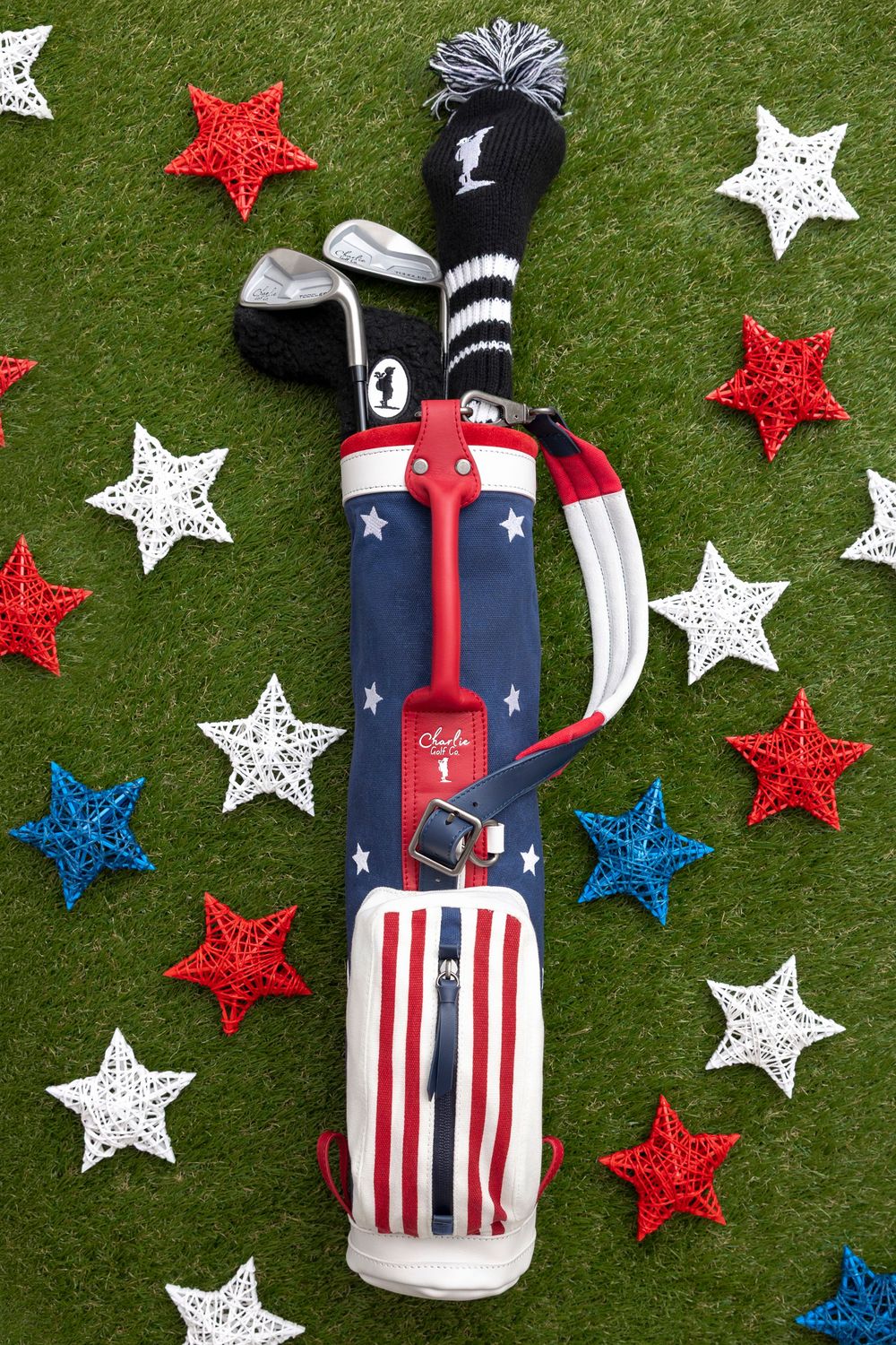 Patriotic golf bag with stars and stripes design, surrounded by red, white, and blue star decorations on green grass.